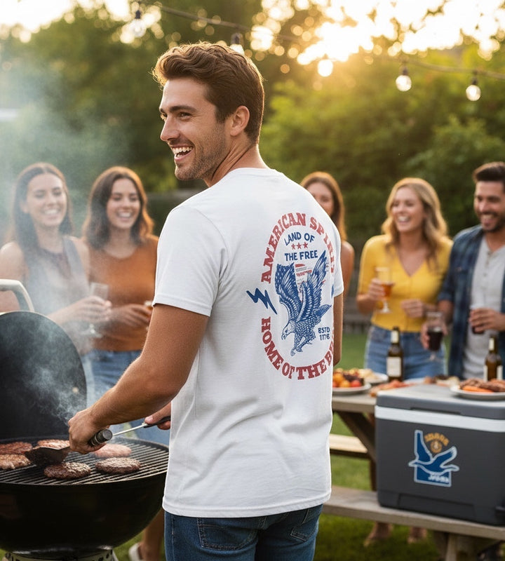JSD Apparel white cotton t-shirt with vintage eagle and patriotic 1776 graphic worn by man at outdoor barbecue