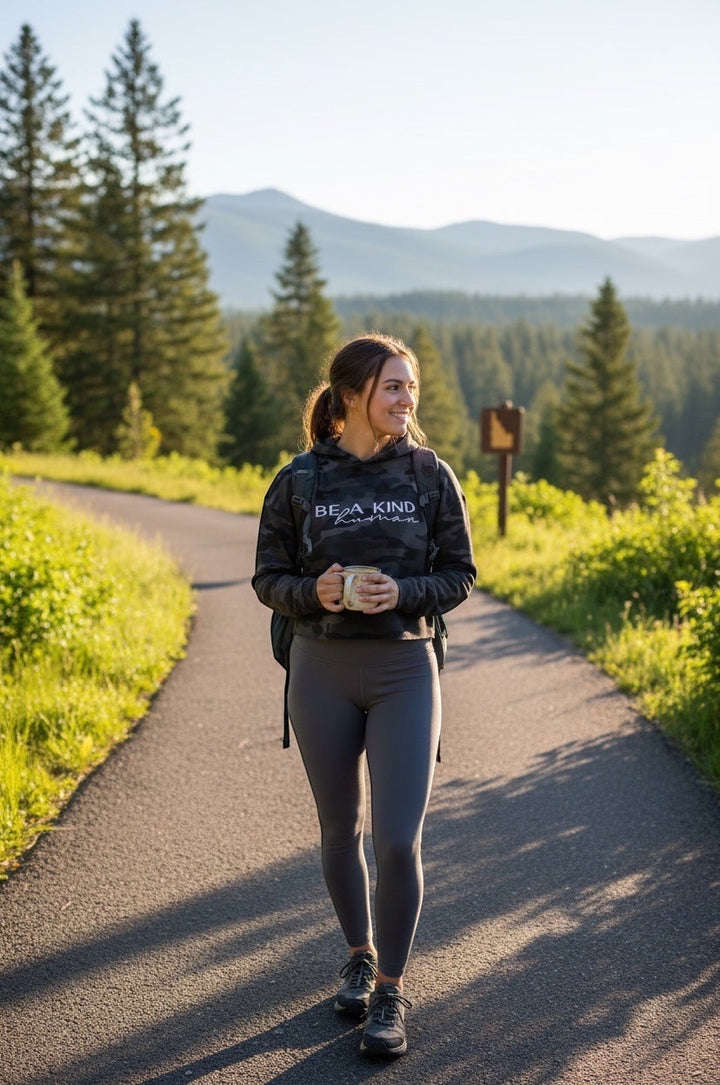 JSD Apparel black camo cropped hoodie with Be A Kind Human text worn by a woman hiking on a mountain trail