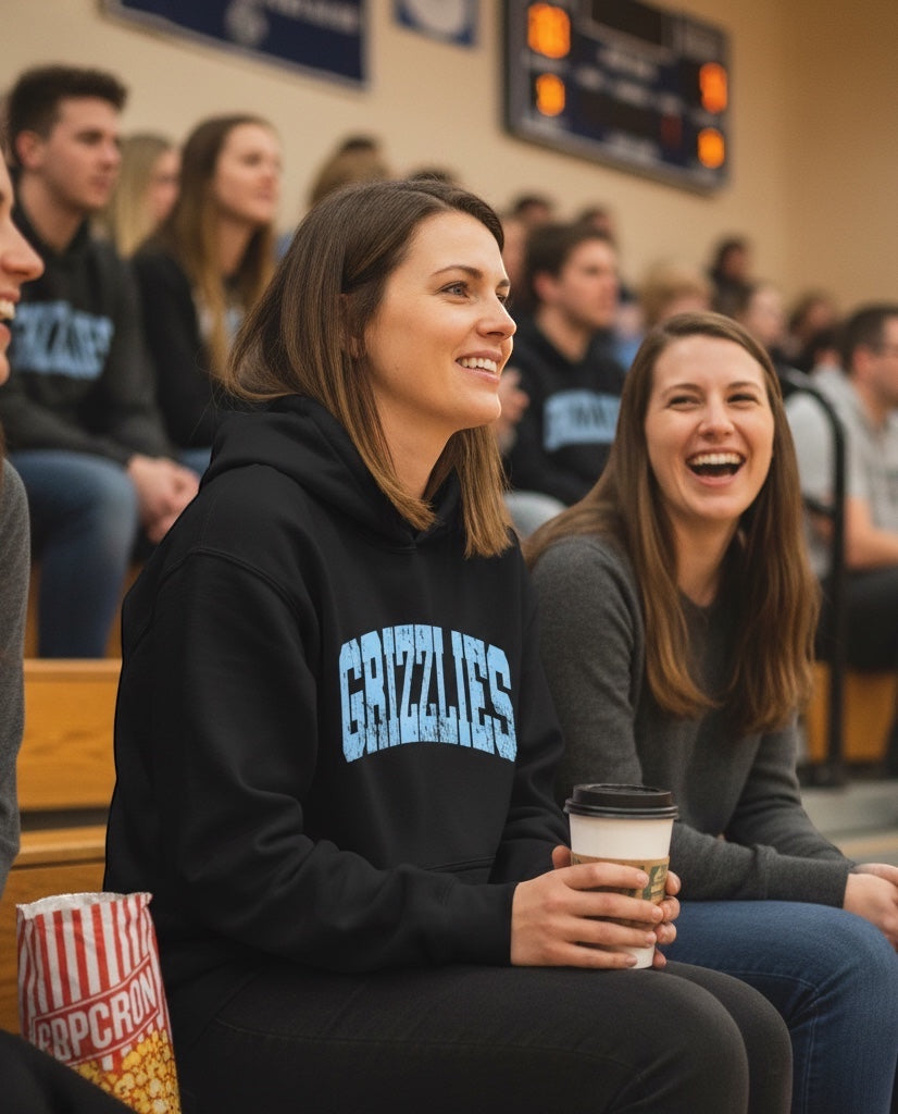 JSD Apparel black heavyweight hoodie with blue distressed Grizzlies arch logo worn by a woman in a stadium