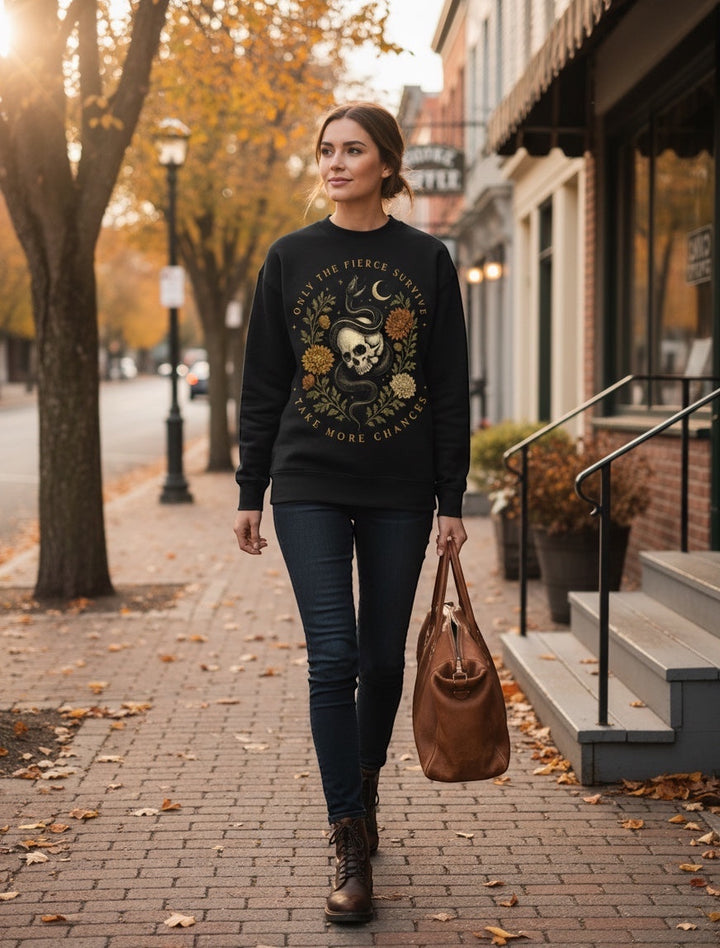 JSD Apparel black mock neck sweatshirt with skull, serpent, and floral graphic worn by a woman on a city sidewalk.