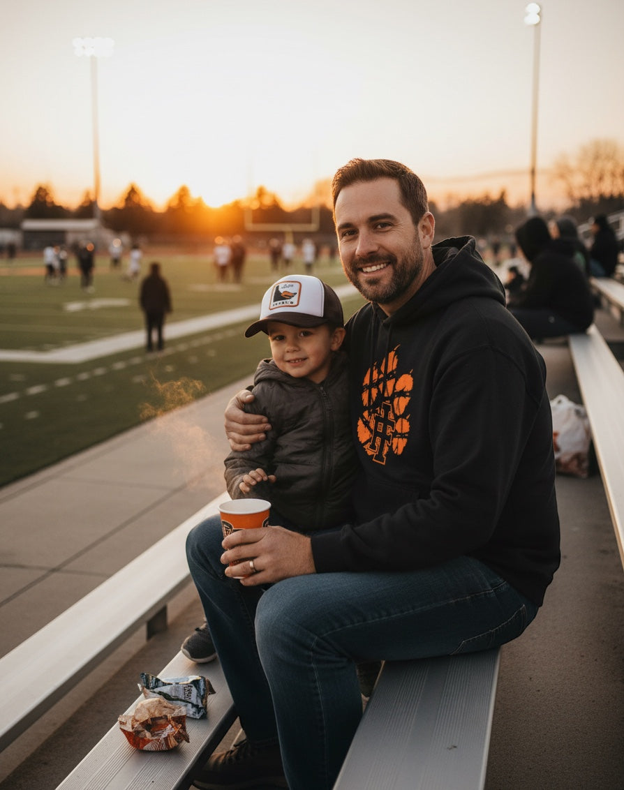 JSD Apparel black heavyweight hoodie with distressed orange tiger paw logo worn by a man at a sunset football game