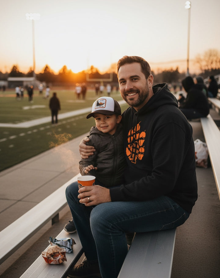 JSD Apparel black heavyweight hoodie with distressed orange tiger paw logo worn by a man at a sunset football game