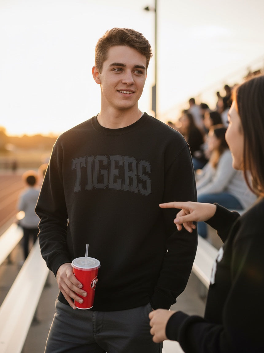 JSD Apparel black crewneck sweatshirt with collegiate TIGERS lettering worn by a young man at a stadium