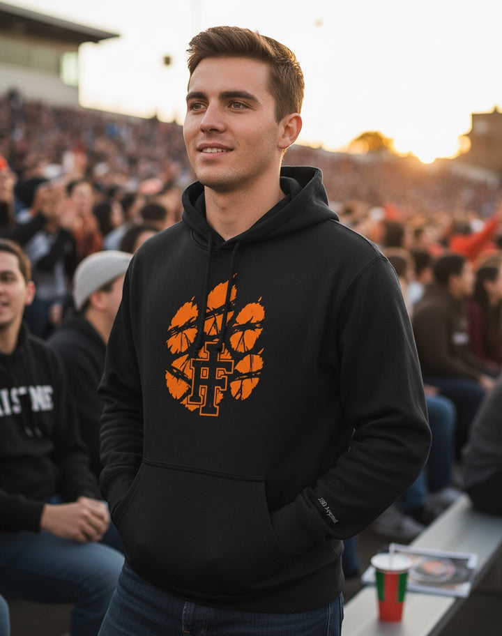 JSD Apparel black heavyweight hoodie with distressed orange Idaho Falls Tigers paw logo worn by a man at a stadium.
