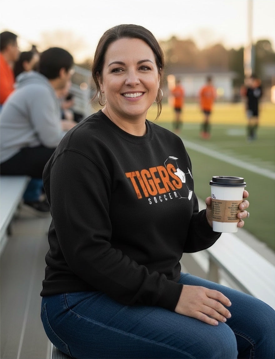 JSD Apparel black vintage crewneck sweatshirt with Tigers Soccer graphic worn by a smiling woman at a soccer field.