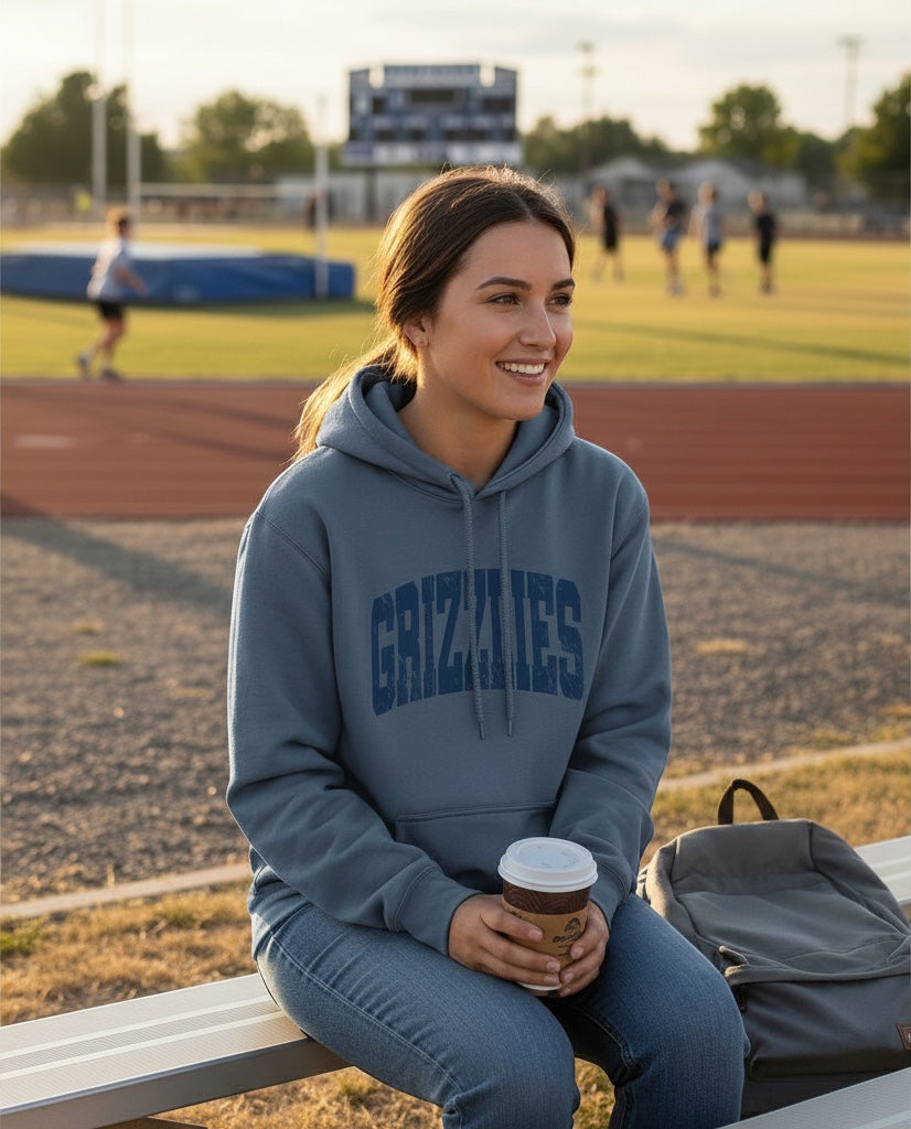 Woman wearing a blue JSD Apparel Skyline Grizzlies heavyweight fleece hoodie with a distressed arch graphic design.