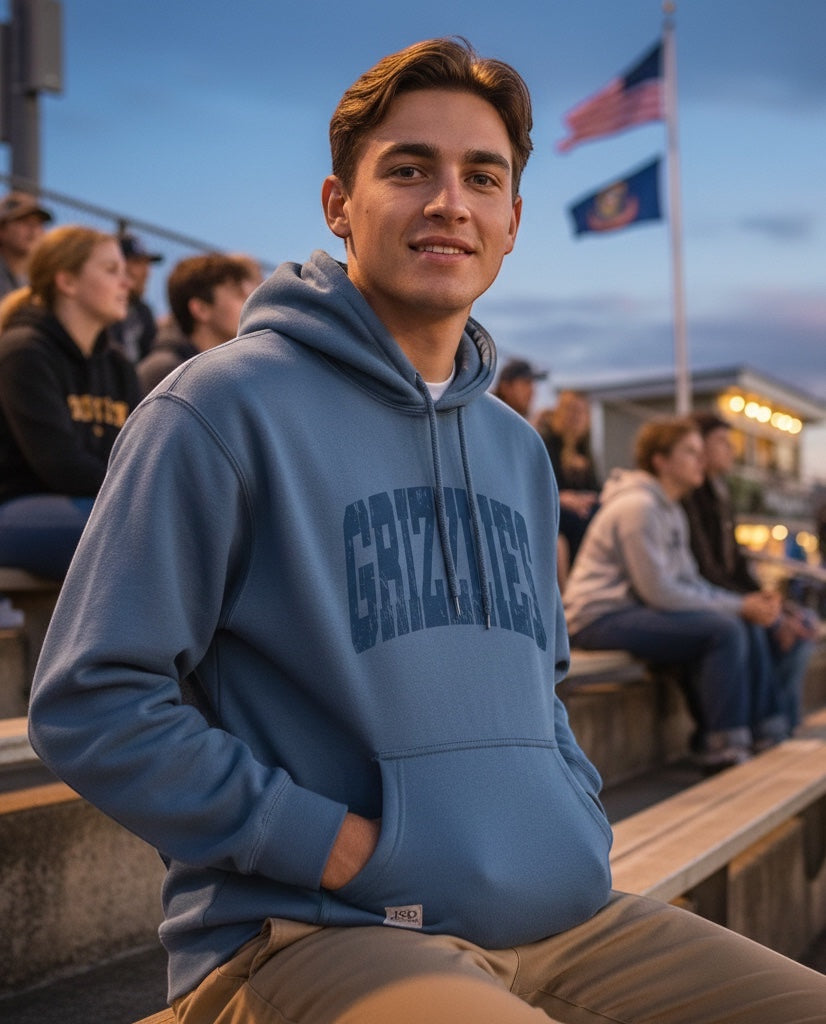 A man wearing a blue JSD Apparel Skyline Grizzlies heavyweight fleece hoodie with a distressed arch graphic design.