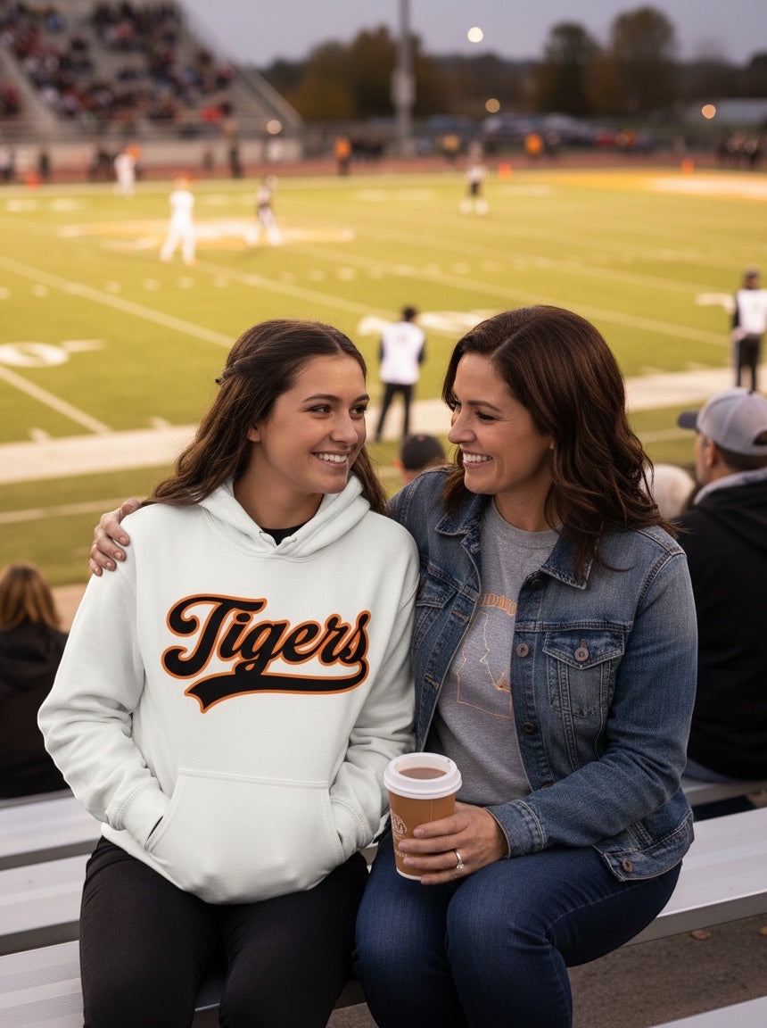 JSD Apparel bone heavyweight hoodie with Tigers script graphic worn by a young woman at a football game