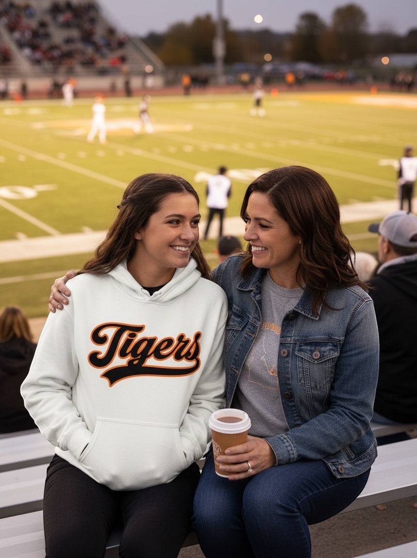 JSD Apparel bone heavyweight hoodie with Tigers script graphic worn by a smiling woman at a football stadium