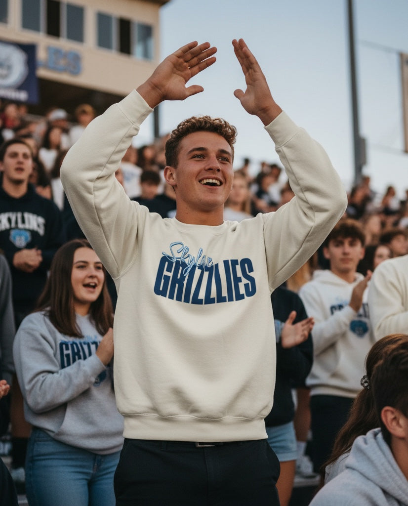 JSD Apparel cream crewneck sweatshirt with blue Grizzlies script logo worn by a cheering student at a stadium