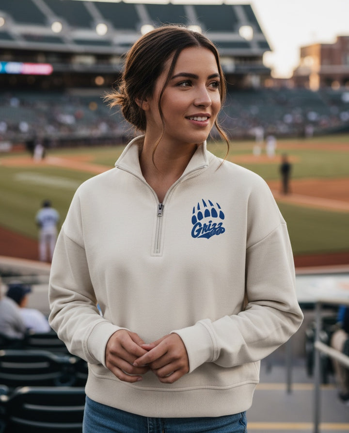Woman wearing a cream JSD Apparel Skyline Grizzlies quarter zip fleece pullover with a blue paw logo at a baseball game