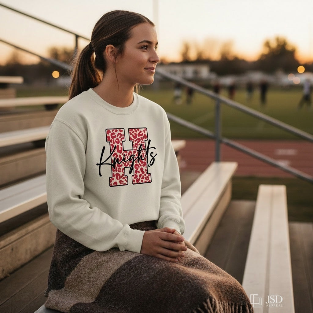 JSD Apparel cream heavyweight crewneck sweatshirt with red leopard-print H and black Knights script on a student