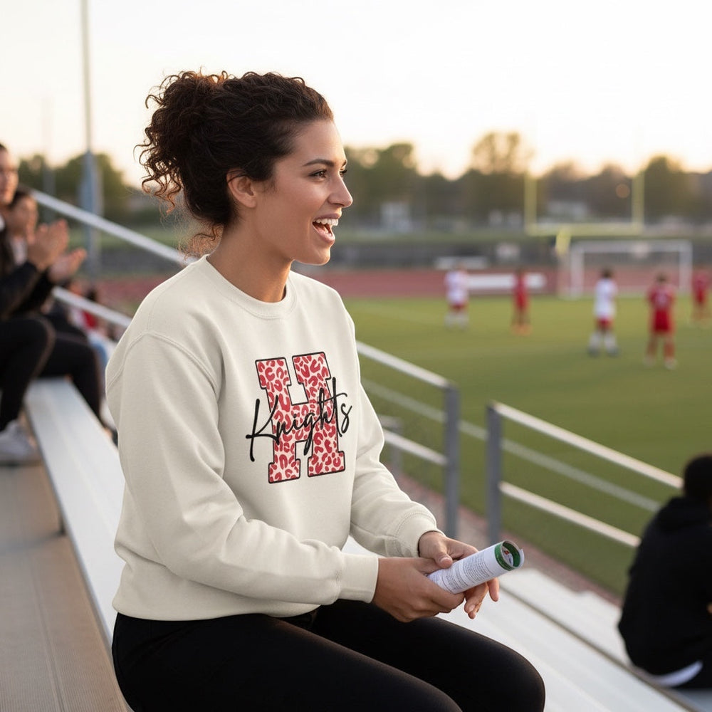 JSD Apparel cream heavyweight crewneck sweatshirt with red leopard-print H and black Knights script at a sports game