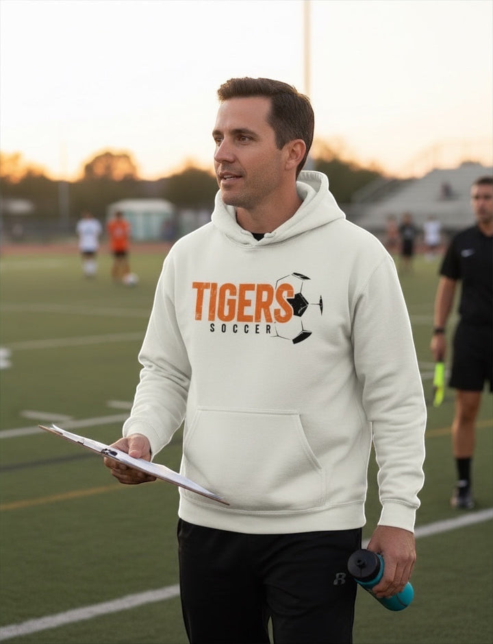 JSD Apparel heavyweight hoodie in cream with orange and black TIGERS soccer graphic worn by a coach on a soccer field