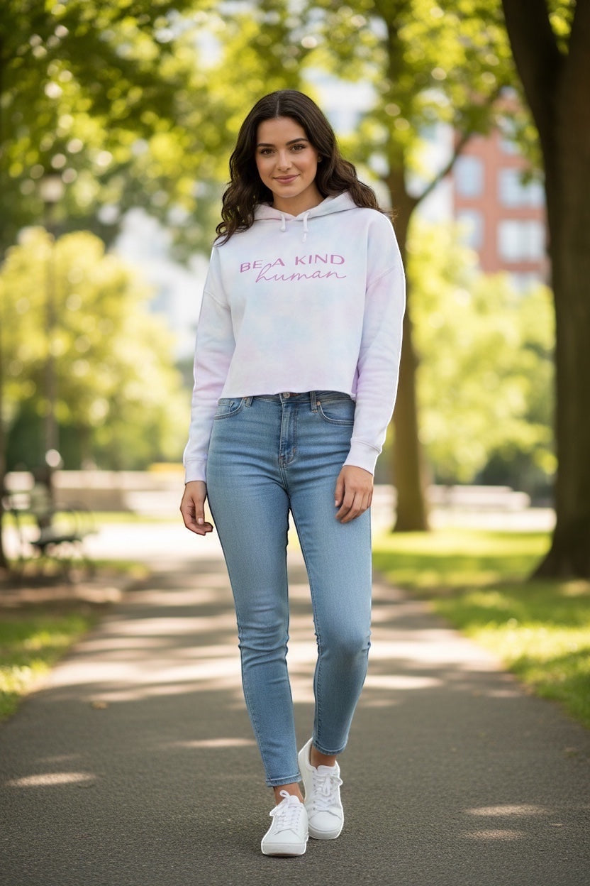 Model wearing a JSD Apparel cropped hooded sweatshirt with Be A Kind Human text in a park setting.