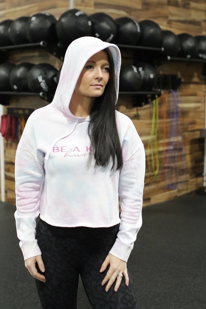 JSD Apparel Be A Kind Human cropped tie-dye hoodie worn by a woman in a gym setting.