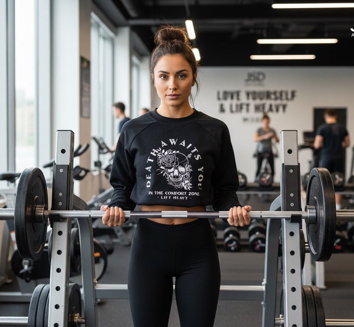 JSD Apparel black cropped fleece pullover with skull graphic, worn by a woman lifting a barbell in a gym.