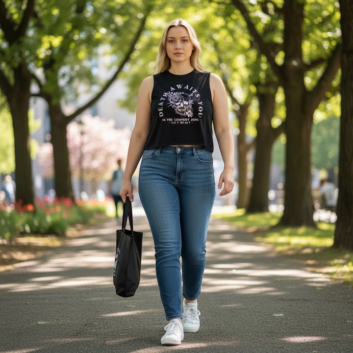 A woman wearing a black JSD Apparel cropped tank with a skull graphic, paired with blue jeans and white sneakers.