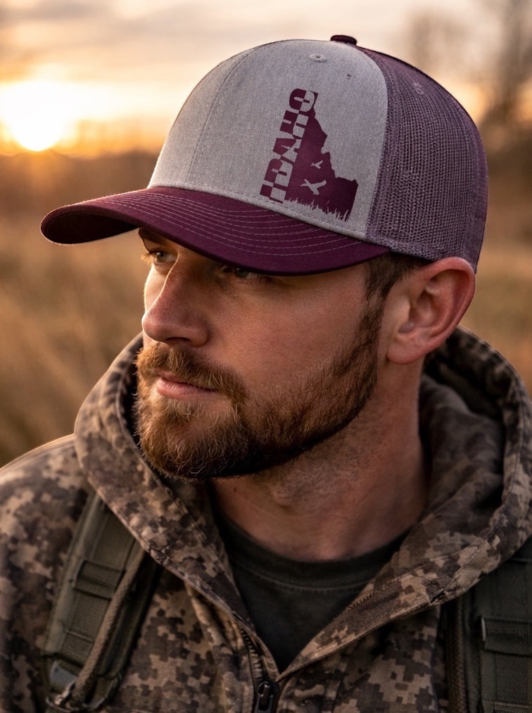 JSD Apparel Flyway Idaho 112 trucker hat in burgundy and heather gray with a duck-themed Idaho state silhouette.