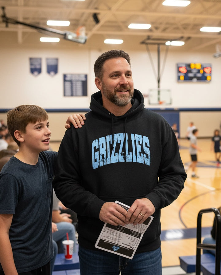JSD Apparel black heavyweight hoodie with distressed light blue Grizzlies arch text worn by a man at a basketball game