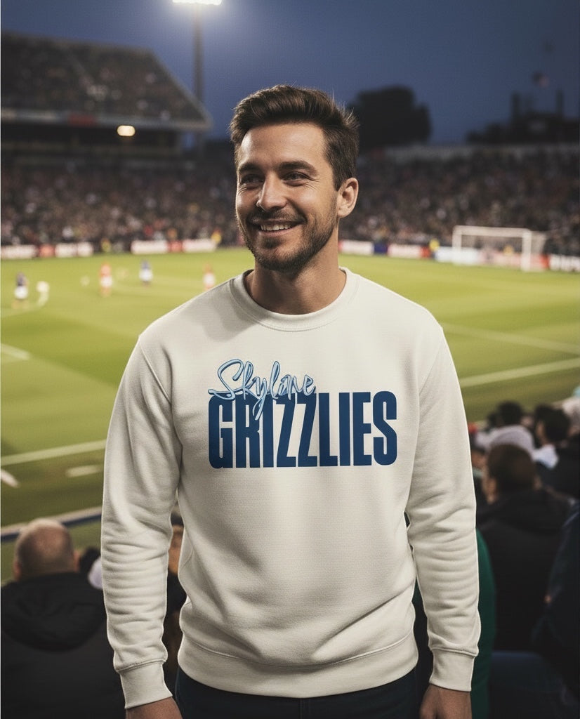 Man wearing JSD Apparel Skyline Grizzlies cream crewneck sweatshirt with blue graphic at a stadium game