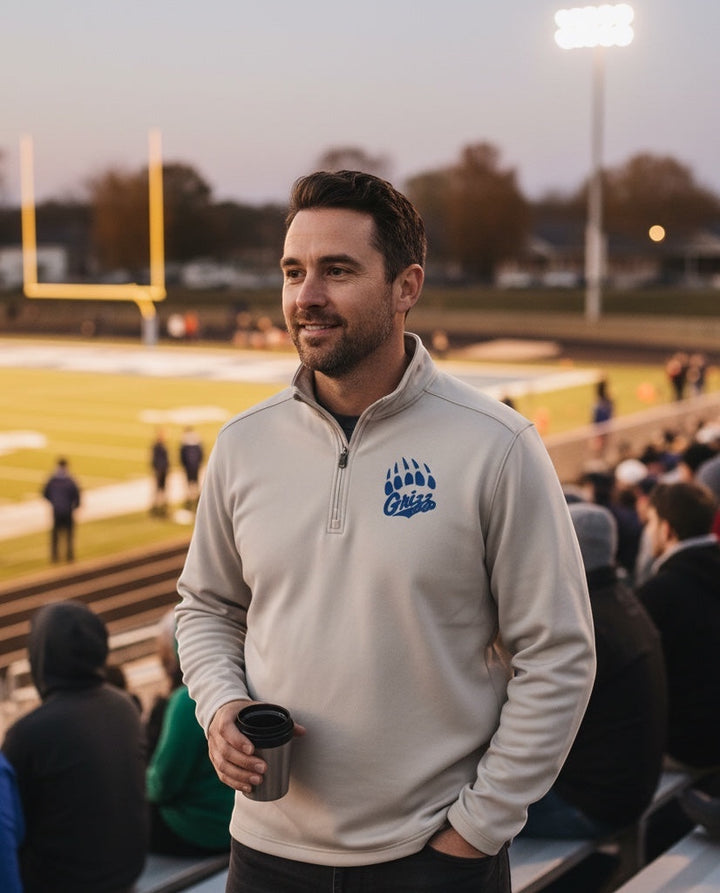 Man wearing a JSD Apparel beige midweight fleece quarter zip pullover with a blue Grizzlies paw logo at a stadium.