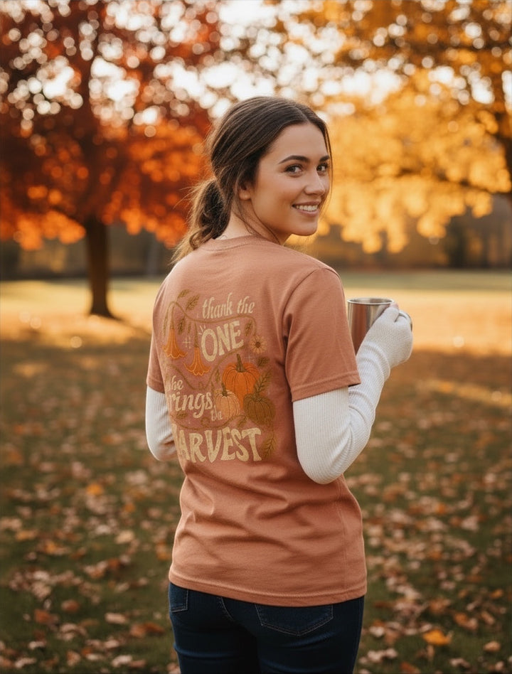 JSD Apparel harvest-themed graphic tee with autumn pumpkin and floral design on a woman in a park setting.