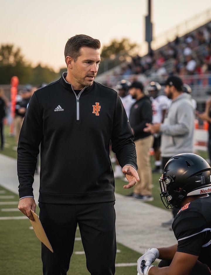 JSD Apparel Idaho Falls Adidas black quarter-zip pullover worn by a coach on a football field