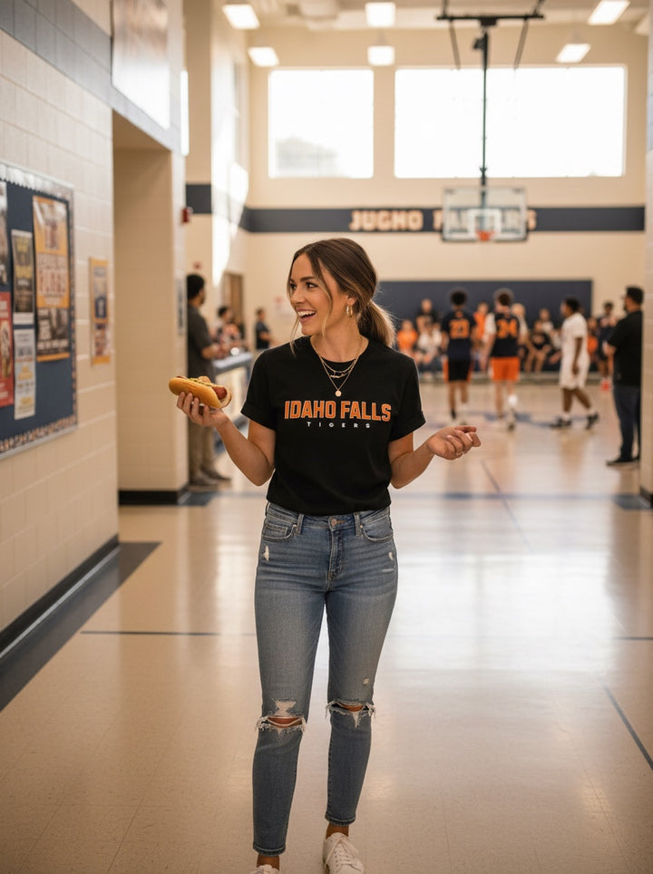 JSD Apparel Idaho Falls Tigers black cotton student tee worn by a smiling woman in a school hallway