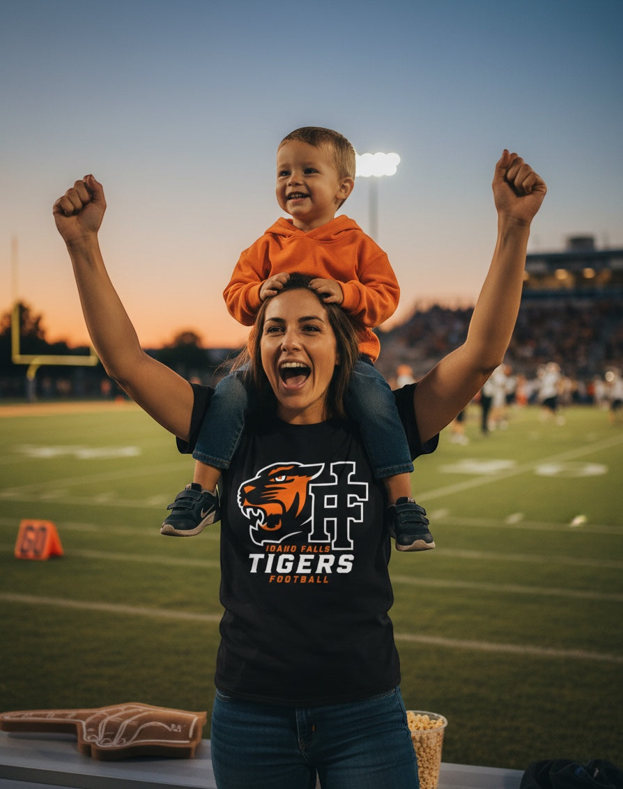 JSD Apparel black Idaho Falls Tigers Football crewneck tee with tiger logo worn by a woman carrying a child on shoulders