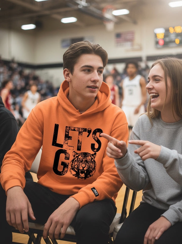 Young man wearing an orange JSD Apparel Idaho Falls Tigers hoodie with a distressed tiger graphic at a basketball game