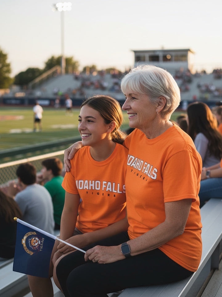 JSD Apparel Idaho Falls Tigers orange cotton t-shirt worn by a smiling student and woman at a football game