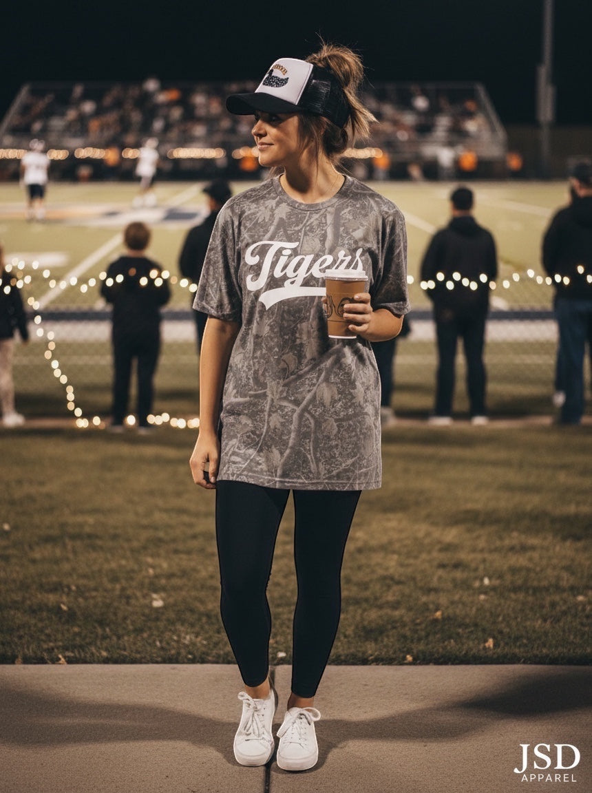 JSD Apparel Idaho Falls Tigers grey pigment-dyed cotton script tee worn by a woman at a night football game.