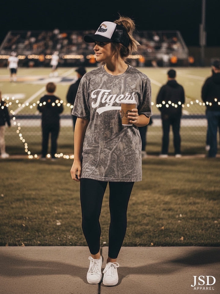 JSD Apparel Idaho Falls Tigers grey pigment-dyed cotton script tee worn by a woman at a night football game.