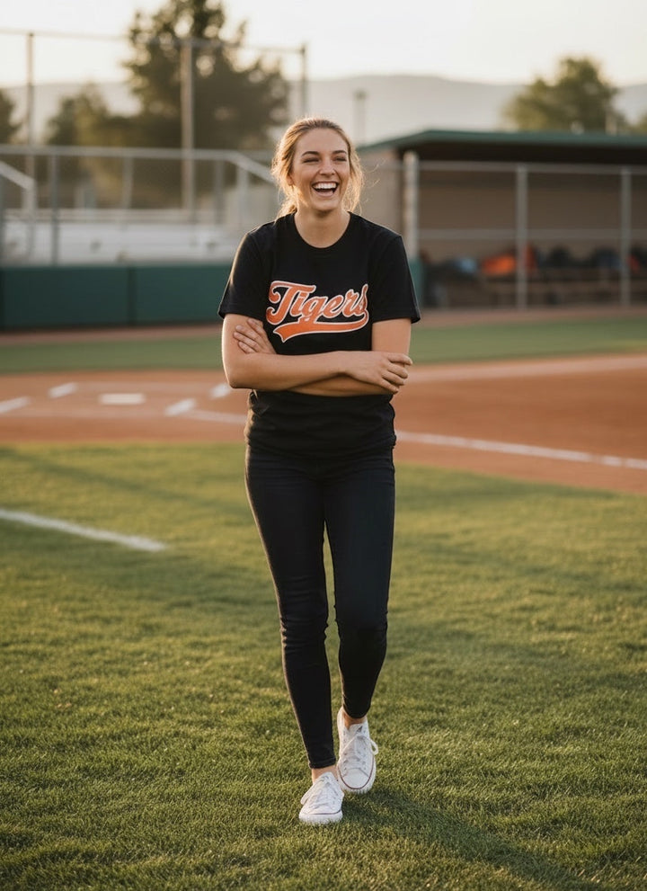 Woman laughing on a baseball field wearing a black JSD Apparel Idaho Falls Tigers cotton script tee.