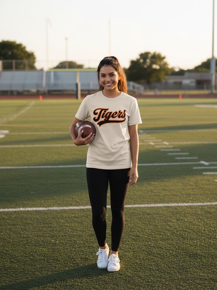 Woman wearing a JSD Apparel Idaho Falls Tigers premium cotton tee with script logo on a football field.