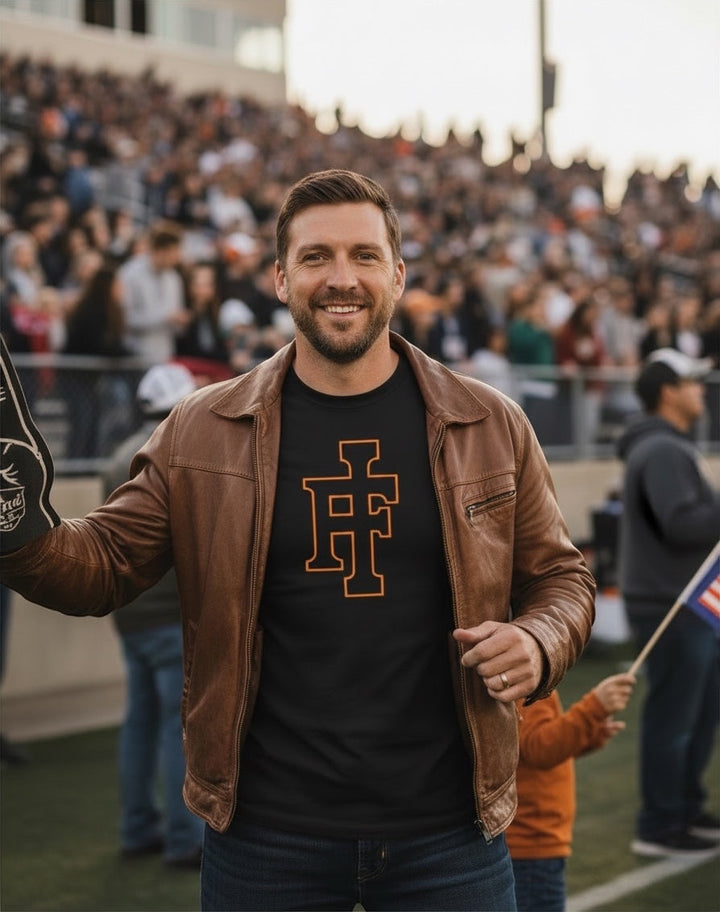 JSD Apparel black premium tee with orange IF logo worn by a man in a brown leather jacket at a stadium