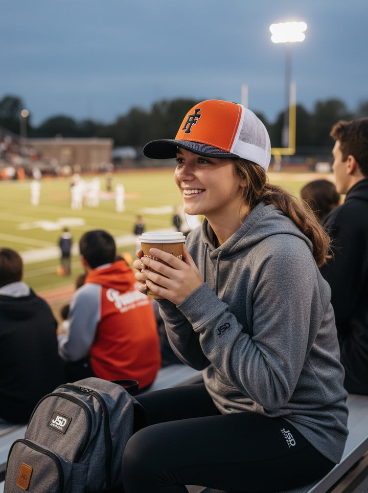 JSD Apparel Idaho Falls Tigers Richardson 112 trucker hat in orange and white worn by a fan at a football stadium.