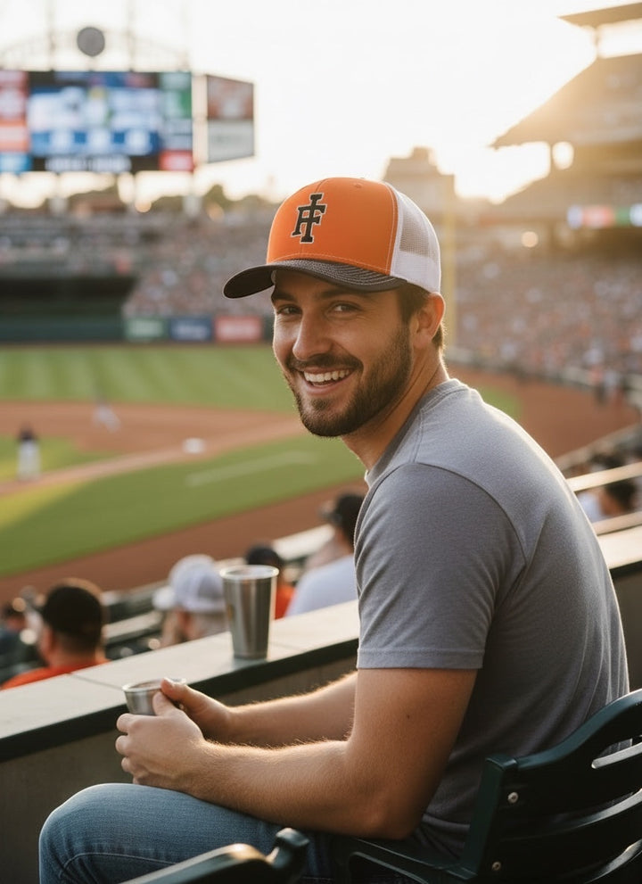 JSD Apparel Idaho Falls Tigers Richardson 112 trucker hat in orange and white worn by a man at a baseball stadium.