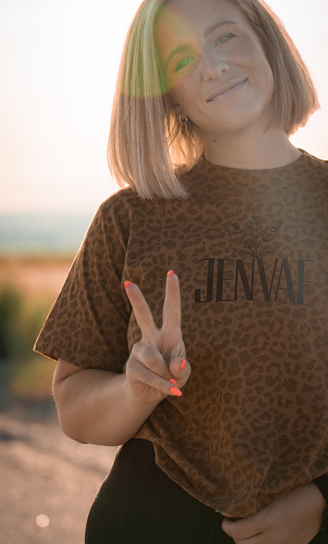 JSD Apparel Jenvae leopard print boxy crop tee in desert tan with sage branch logo, worn by a woman outdoors.