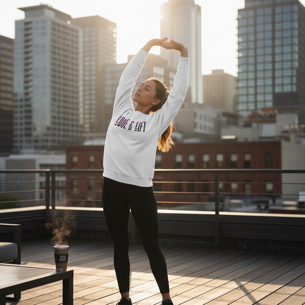 Woman wearing a white JSD Apparel Love & Lift loopback terry crewneck sweatshirt stretching on a city rooftop at sunset