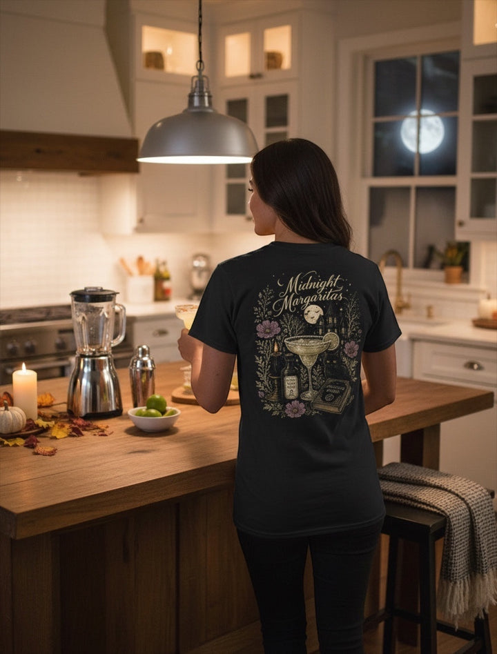 JSD Apparel Midnight Margaritas unisex tee featuring a detailed witchy back graphic in a cozy kitchen setting.