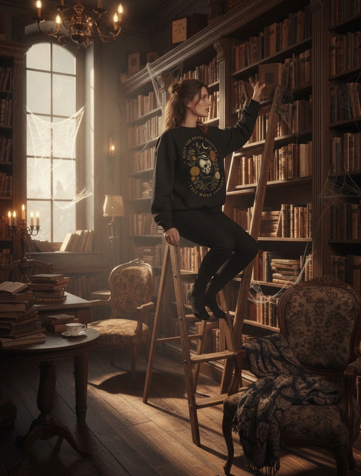 JSD Apparel mock neck sweatshirt with skull and serpent graphic worn by a woman on a library ladder