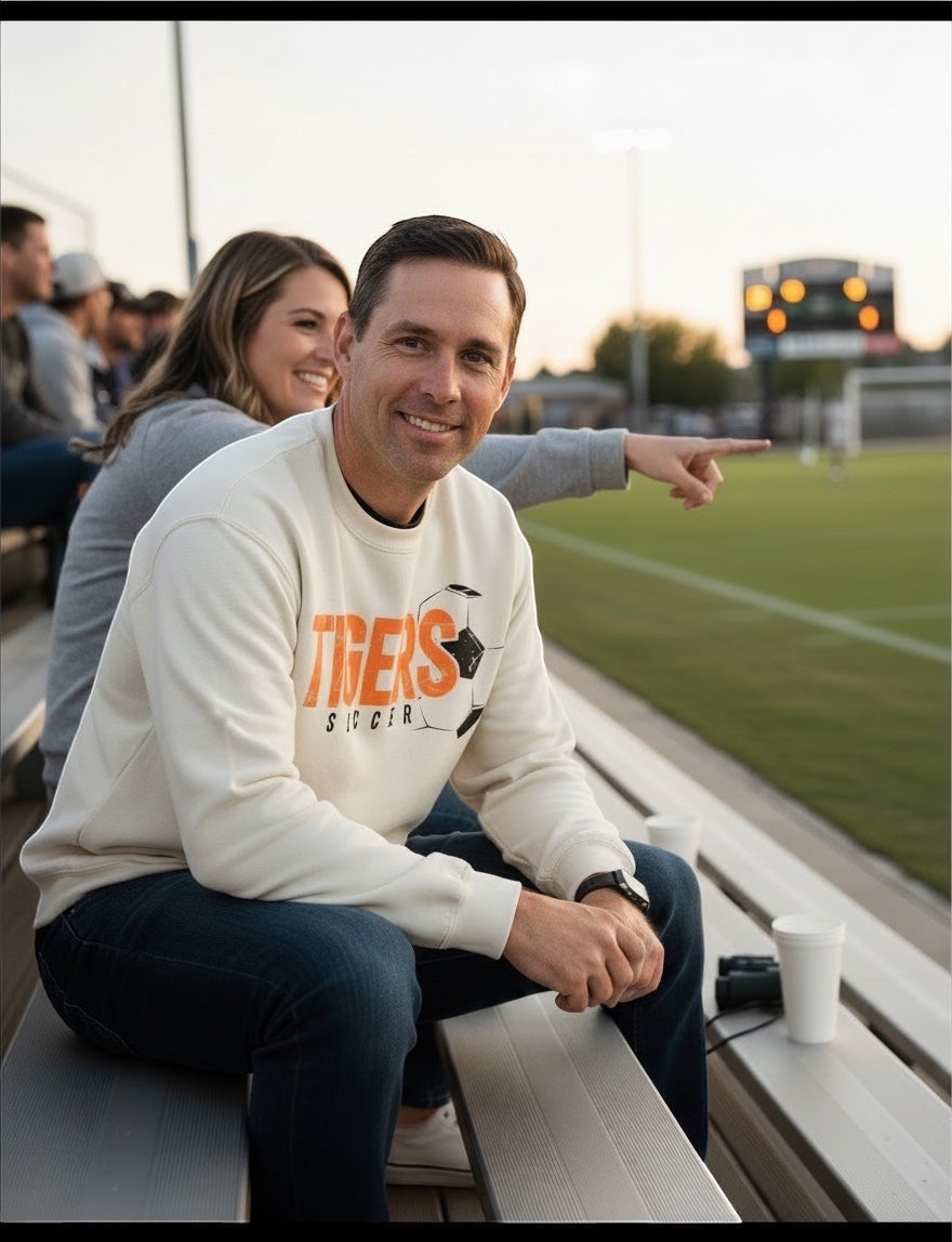 JSD Apparel natural crewneck sweatshirt with distressed orange and black Tigers Soccer graphic worn by a man at a game