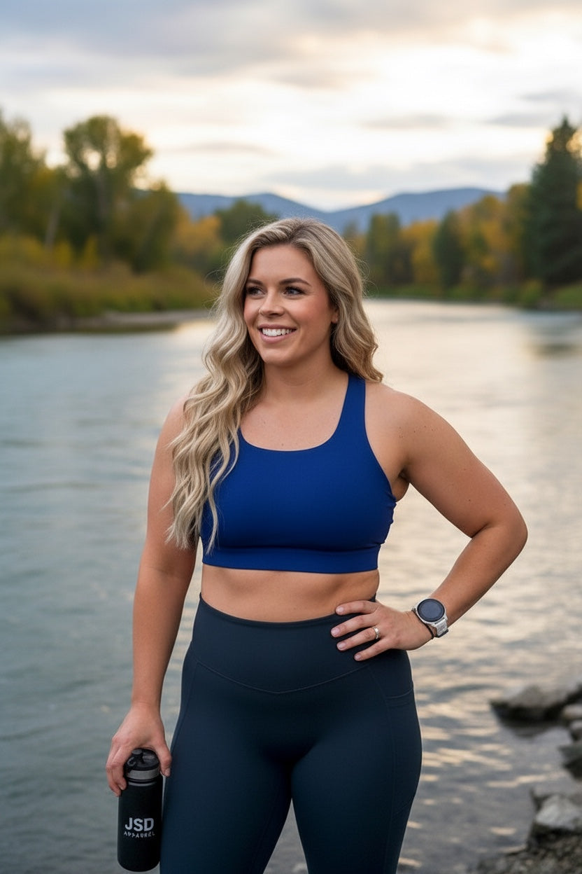 Woman wearing JSD Apparel ocean navy performance sports bra by a river, featuring a longline fit and athletic design.