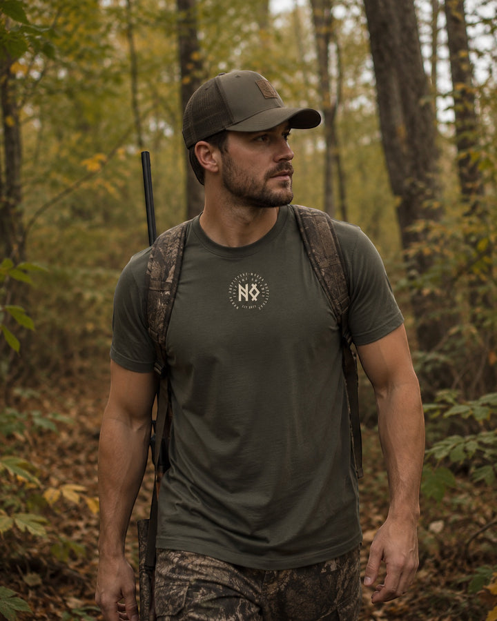 JSD Apparel men's olive green short-sleeve t-shirt with a circular graphic on the chest, worn by a man in a forest setting.