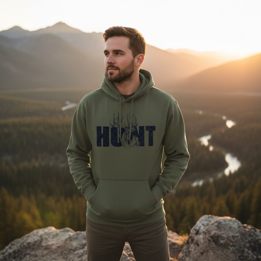 JSD Apparel olive green heavyweight hoodie with HUNT elk graphic worn by a man overlooking a mountain valley at sunset
