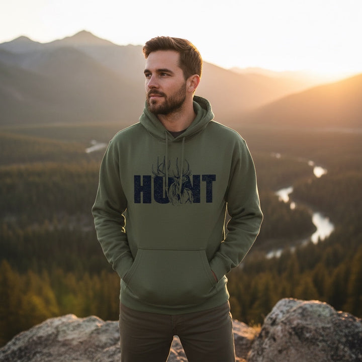 JSD Apparel olive green heavyweight hoodie with HUNT elk graphic worn by a man overlooking a mountain valley at sunset