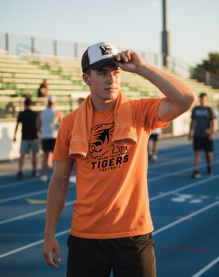 JSD Apparel orange Idaho Falls Tigers football t-shirt worn by a young man on a running track with a matching cap