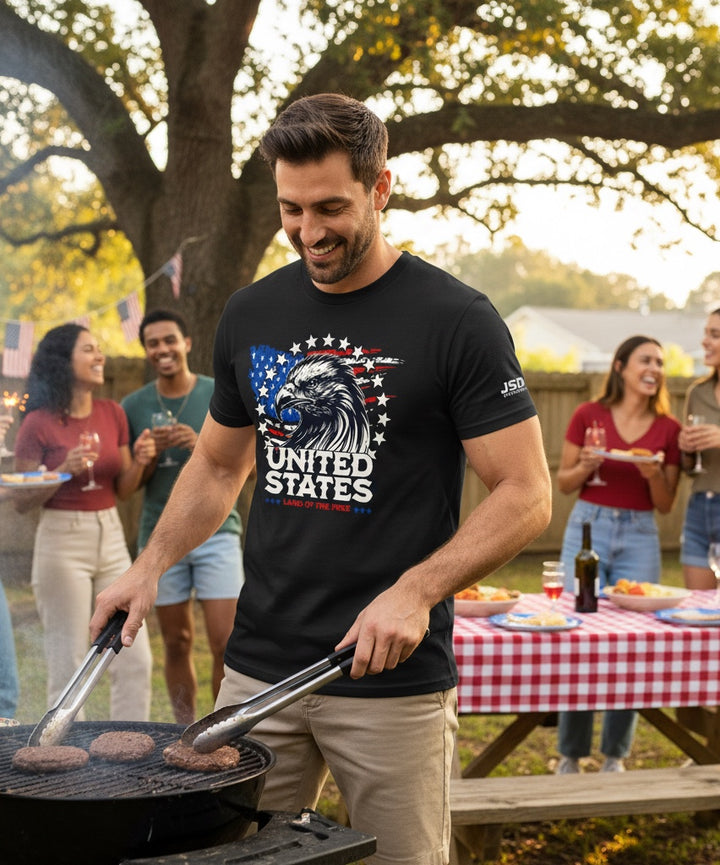 Man wearing a black JSD Apparel t-shirt with a patriotic bald eagle and American flag graphic at a backyard barbecue.